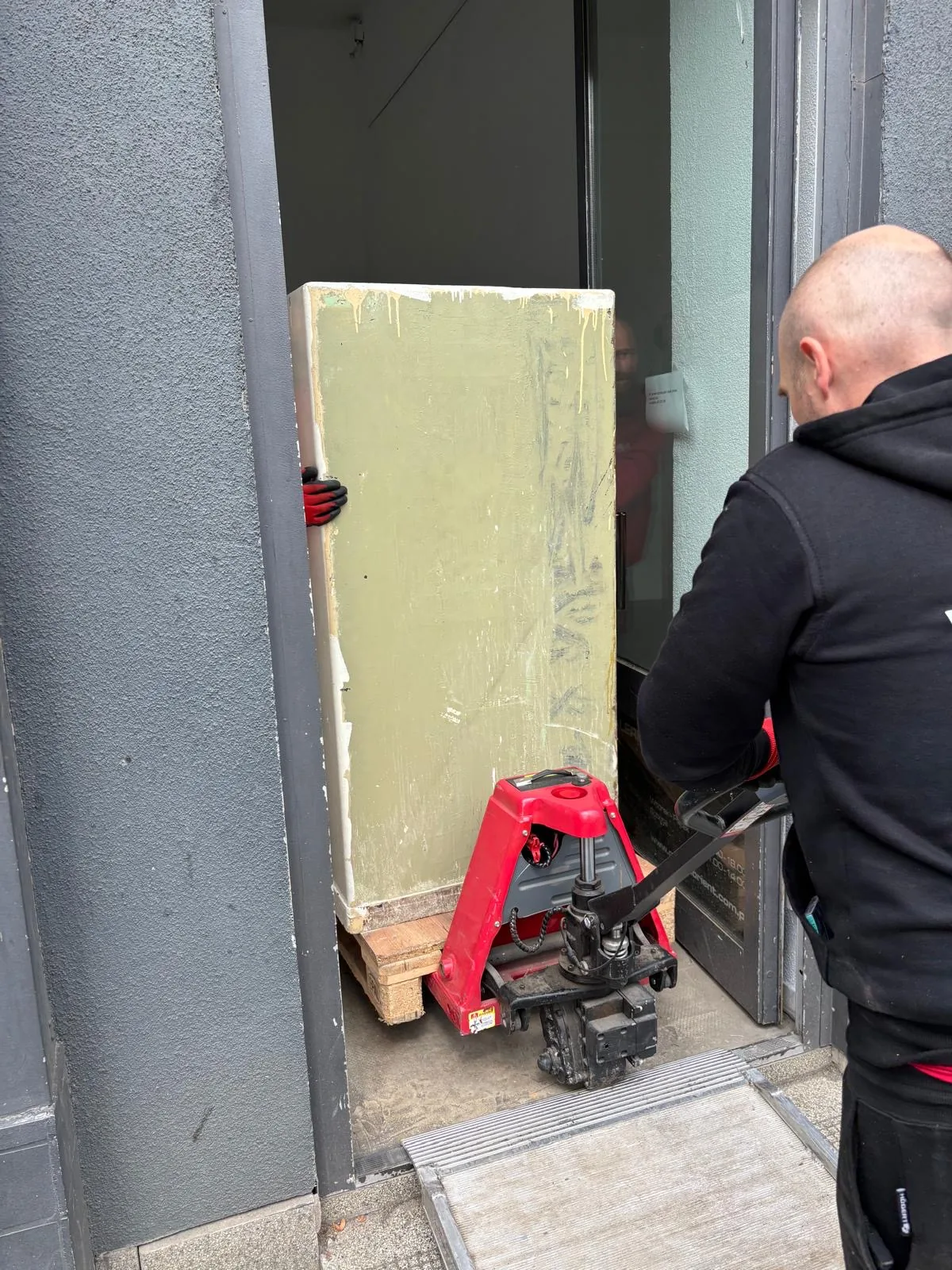 Przejazd sejfu na wózku paletowym przez wąskie drzwi wejściowe lokalu po rampie progowej