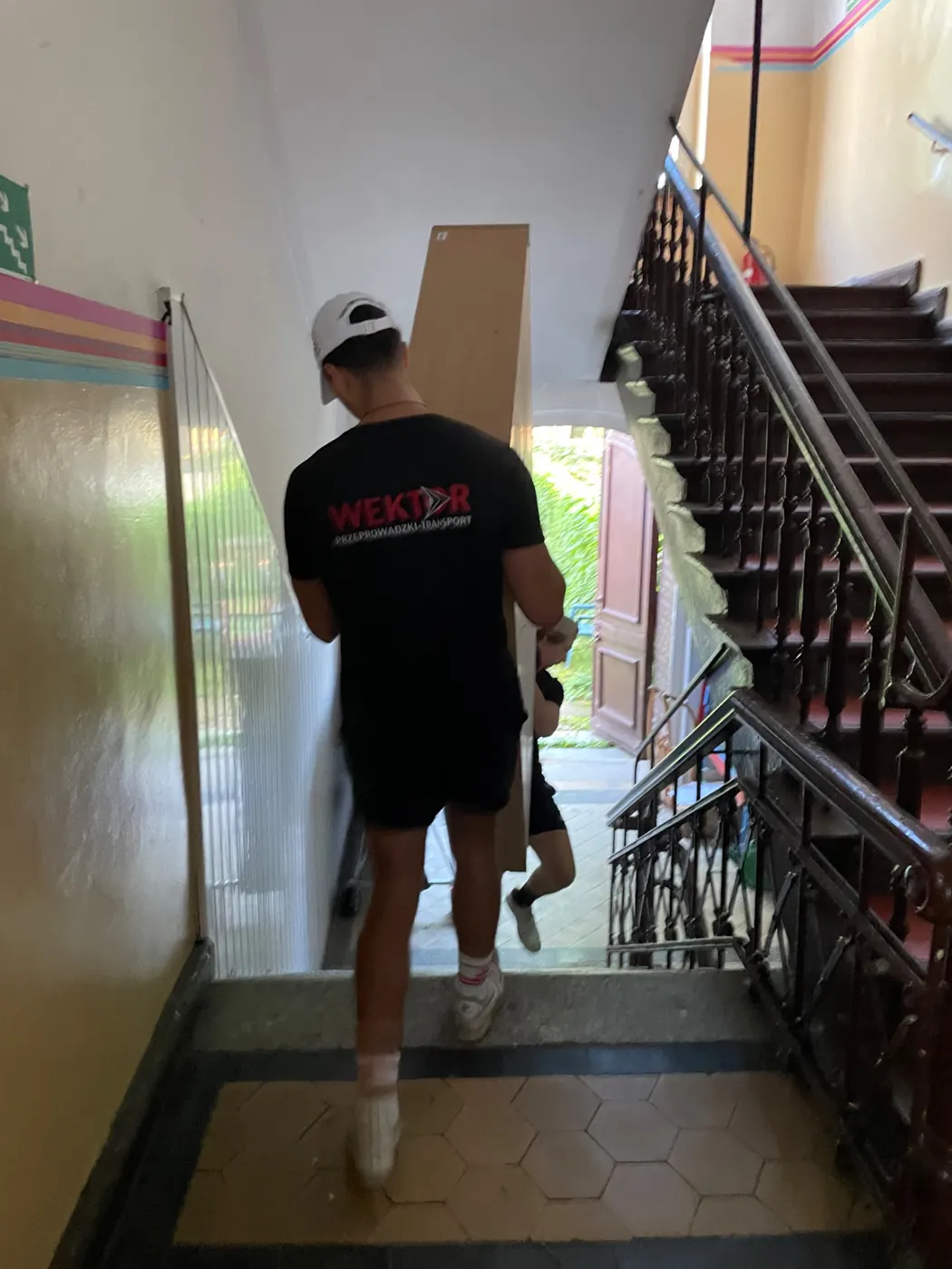 Pracownik Wektor w firmowej koszulce znosi blat mebla klatką schodową Szkoły Podstawowej nr 67 w Szczecinie